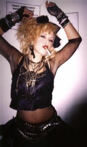 Young woman dressed as mid 80's Madonna. All black clothing, tousled hair, midriff net lace, and many necklaces and bracelets with black bow in hair.