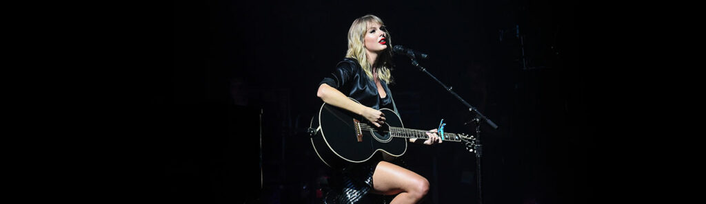 Taylor Swift in black dress with black guitar on stage