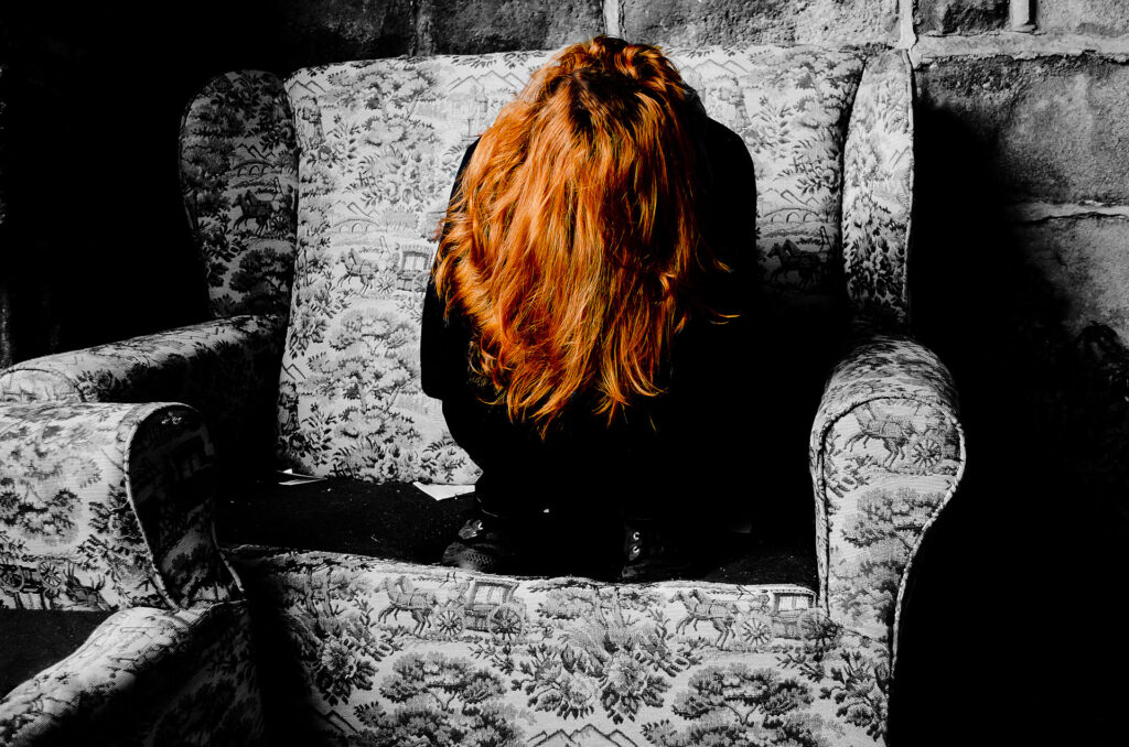 A woman huddled in a chair crying with her hair covering her face