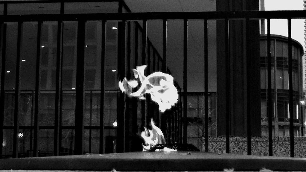 Eternal memorial flame with city buildings in the background. Black and white.