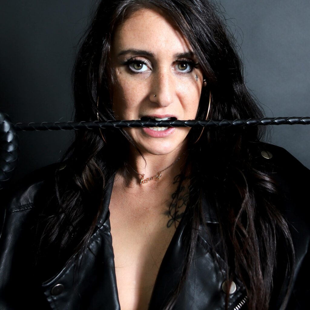 Woman in leather jacket and a whip in her teeth
