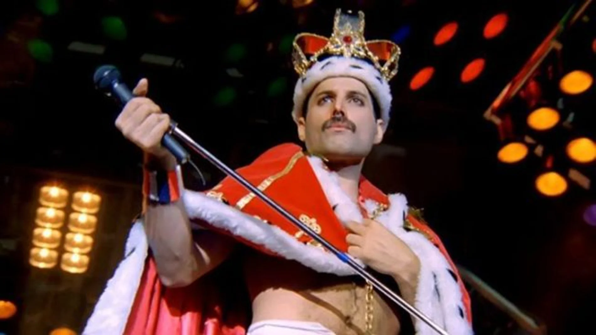 Freddie Mercury on stage wearing a red crown and red cape
