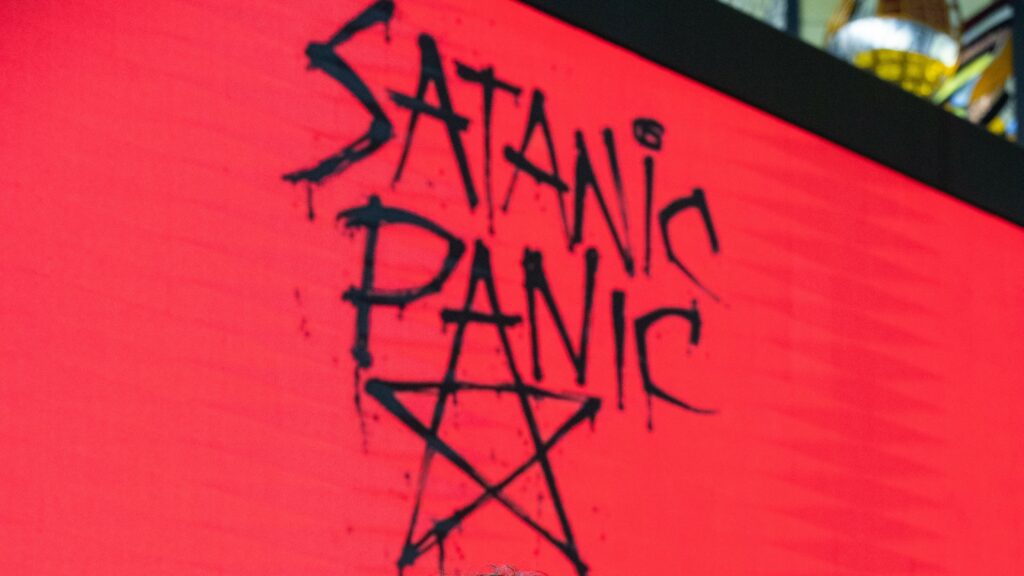 Words "Satanic Panic" above a pentagram in black spray-paint on a red background