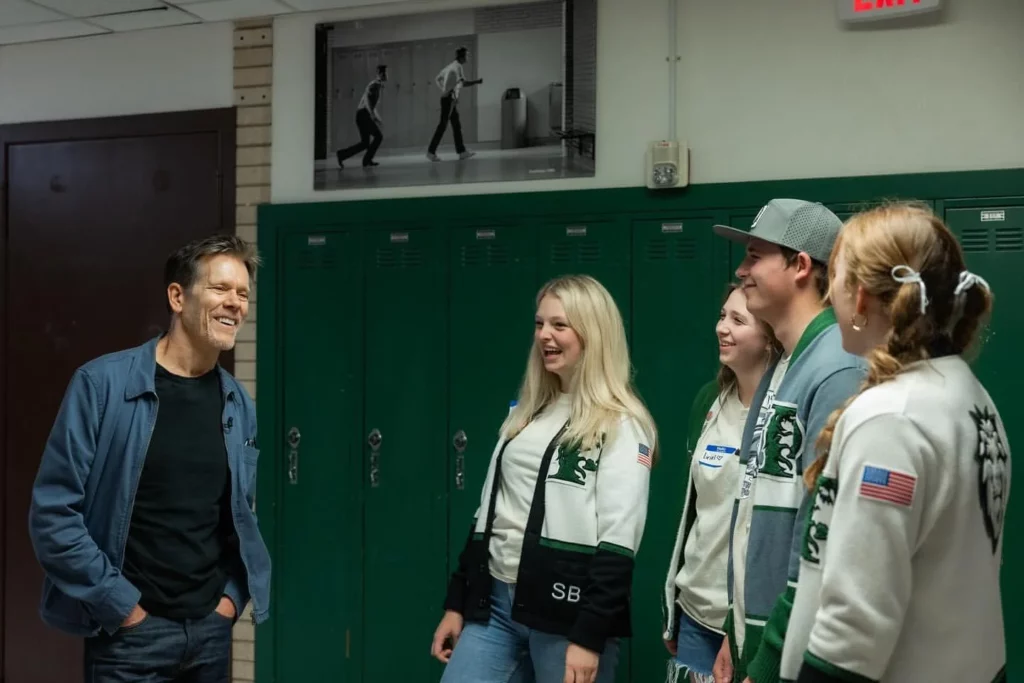 Kevin Bacon by a high school locker laughing with 4 high school students