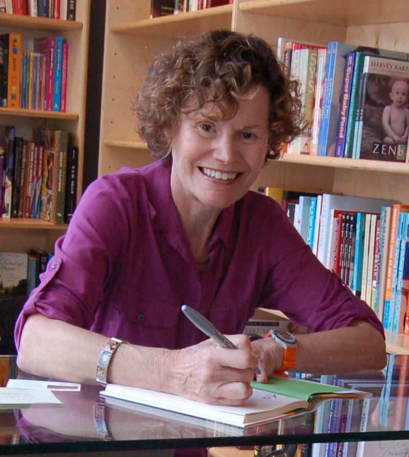 Judy Blume sitting at a desk smiling as the signs a book.