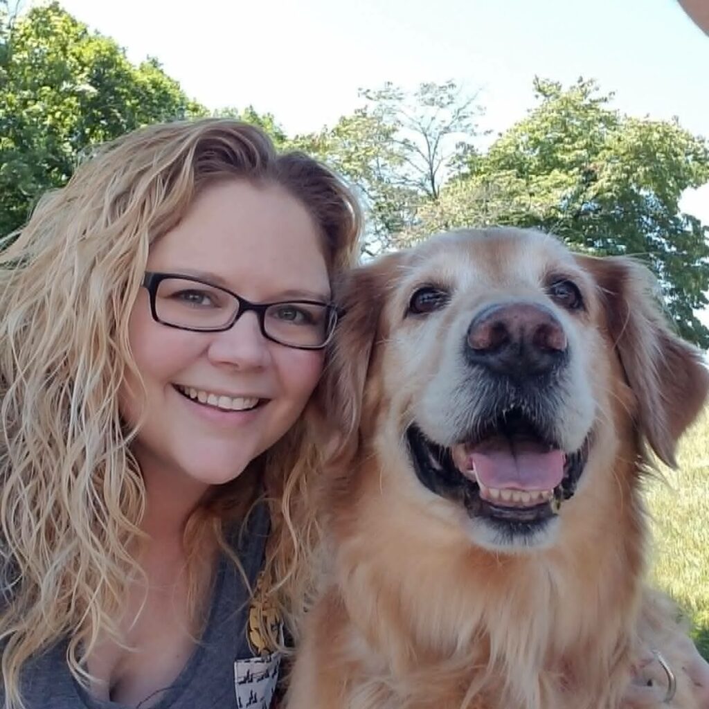 Blonde woman with glasses smiling next to a large dog. 