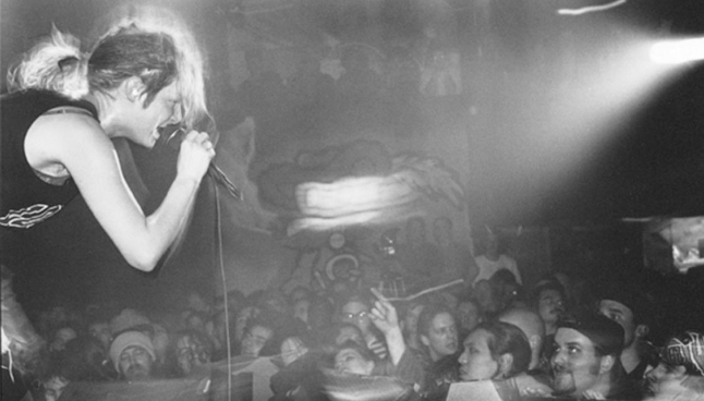 Woman on stage singing with a microphone in hand as audience watches