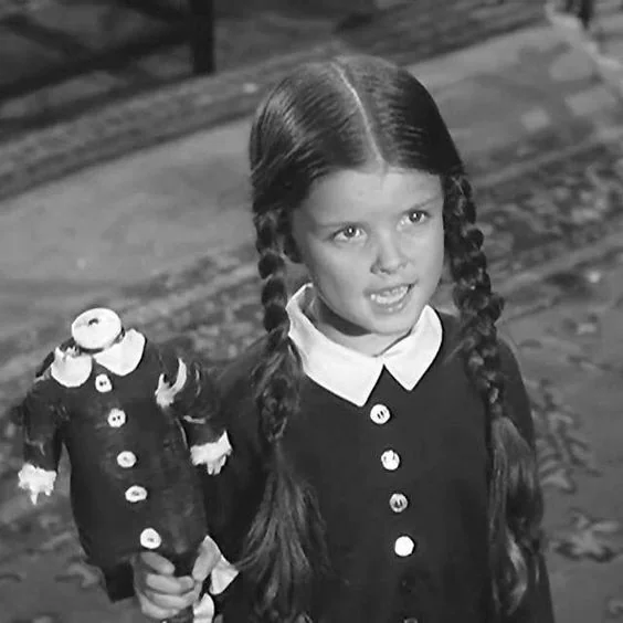 Wednesday Addams holding a headless doll.