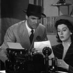 Man and a woman in a newsroom looking at a story they wrote on a typewriter