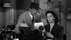 Man and a woman in a newsroom looking at a story they wrote on a typewriter