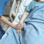 Person in Blue Scrub Suit Holding the Hand of a Patient