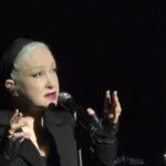 Cyndi Lauper on stage in an all black background.