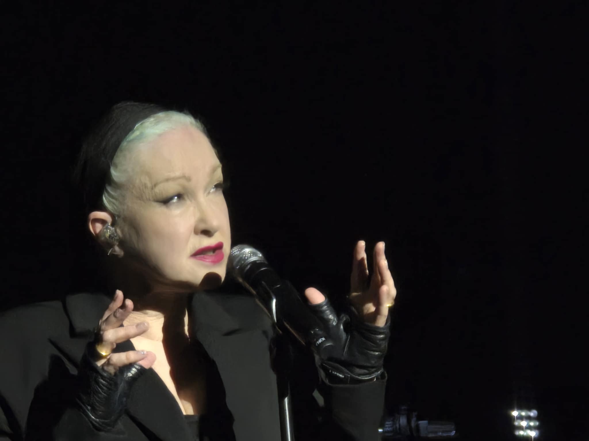 Cyndi Lauper on stage in an all black background.