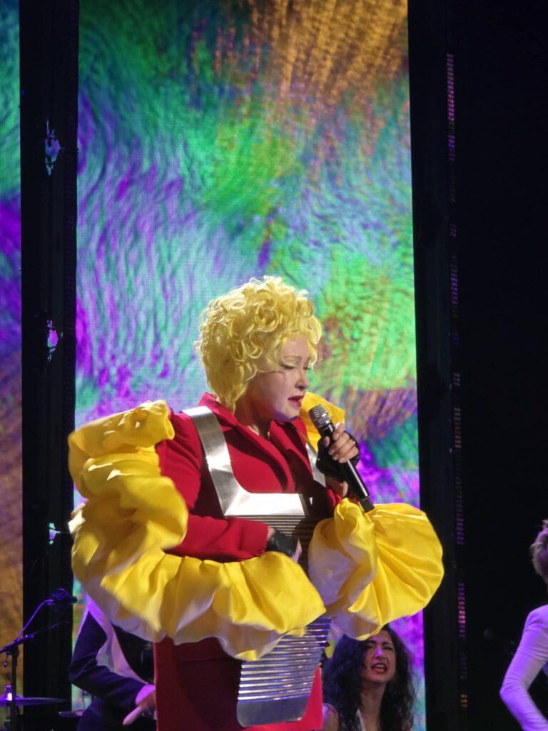 Cyndi Lauper in a yellow and red dress telling stories onstage