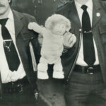 Cabbage Patch doll carried away by 2 police officers