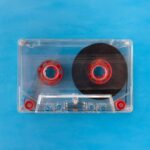 Vintage transparent cassette tape with red reels on a bright blue background.