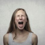 Young woman screaming with emotion, showing braces, against a gray backdrop.