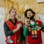 Two men enjoying a holiday party with fun ugly Christmas sweaters and cheerful decorations.