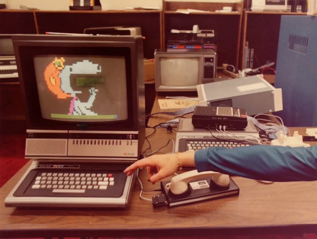 Computer from the 1980s with an old style telephone modem and a finder reaching out for the keyboard.