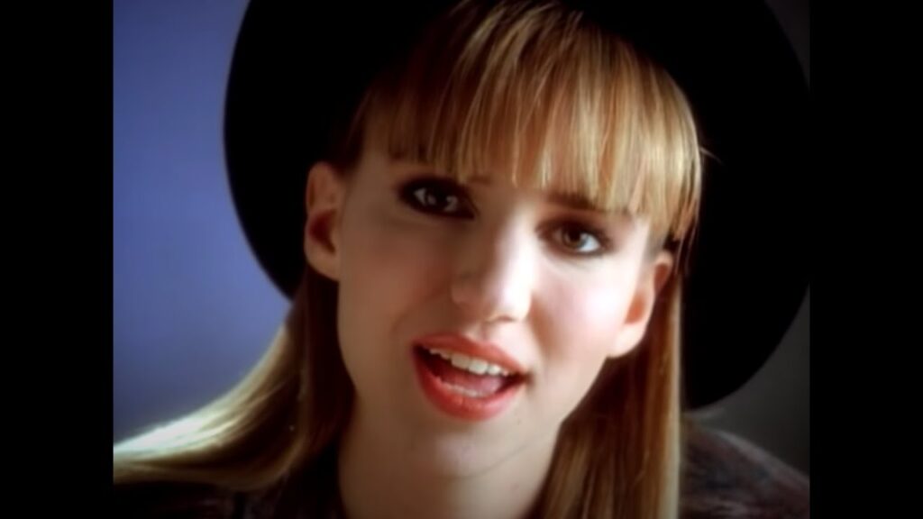 Teenage Debbie Gibson with bangs and a hat looking into the camera singing