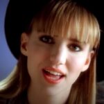 Teenage Debbie Gibson with bangs and a hat looking into the camera singing