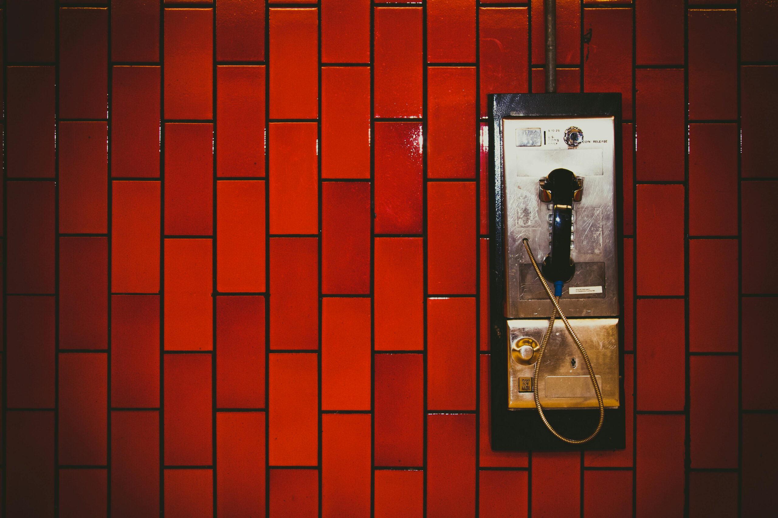 A retro payphone mounted on a vibrant red tiled wall, evoking nostalgia and urban charm.