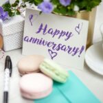 Happy anniversary card with flowers, gift, macarons, and coffee on a table.