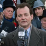 Bull Murray as Phil Conners giving a news report about groundhog day holding a news microphone.