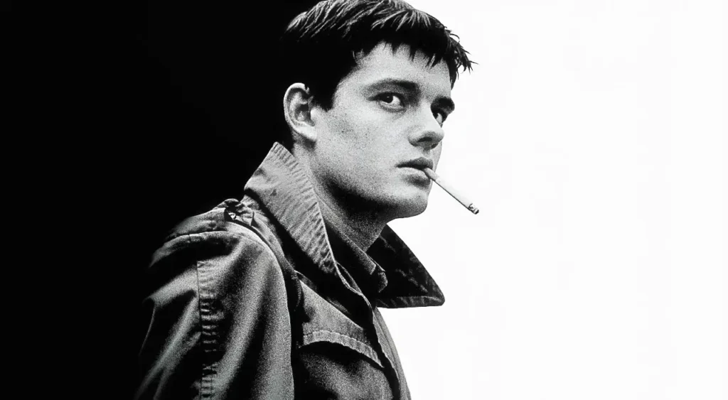 Photo of Ian Curtis smoking a cigarette while wearing a trenchcoat