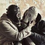 Two individuals wearing gas masks embrace in an urban setting, highlighting themes of protection.