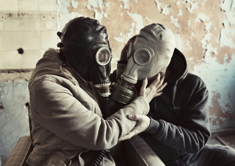 Two individuals wearing gas masks embrace in an urban setting, highlighting themes of protection.